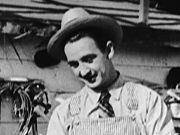 Black-and-white film still of Charles King, a man in a hat and work clothes smiling slightly outdoors.